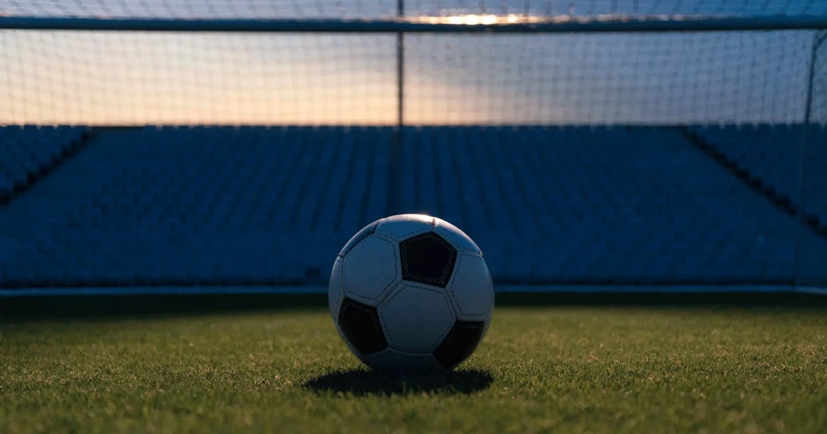 Ein Fußball liegt im Strafraum direkt vor dem Tor mit Netz, im Hintergrund leere Ränge bei Dämmerung.